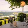 Terrasse mit Tisch, Blumen und Blick auf Flusslandschaft.