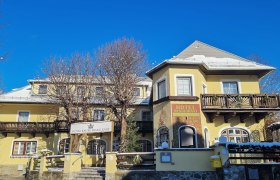 Gelbes Hotelgebäude mit Holzverzierungen und blauen Himmel im Hintergrund.