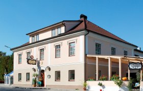 Ein traditionelles Gasthaus mit rosa Fassade und rotem Dach, dekoriert mit Pflanzen und einem K&uuml;rbis.