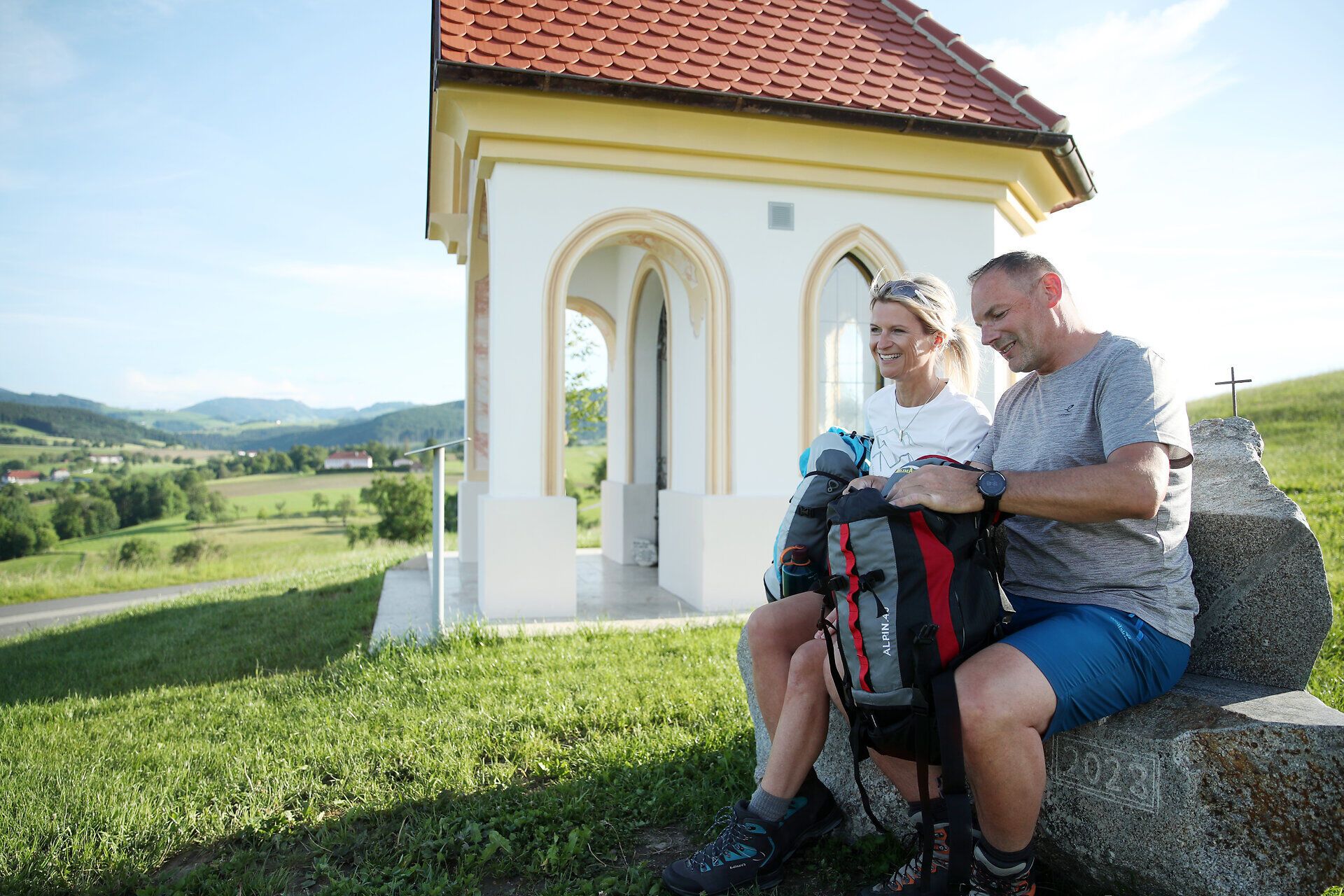 Pilgerpaar rastet bei Kapelle mit Aussicht.