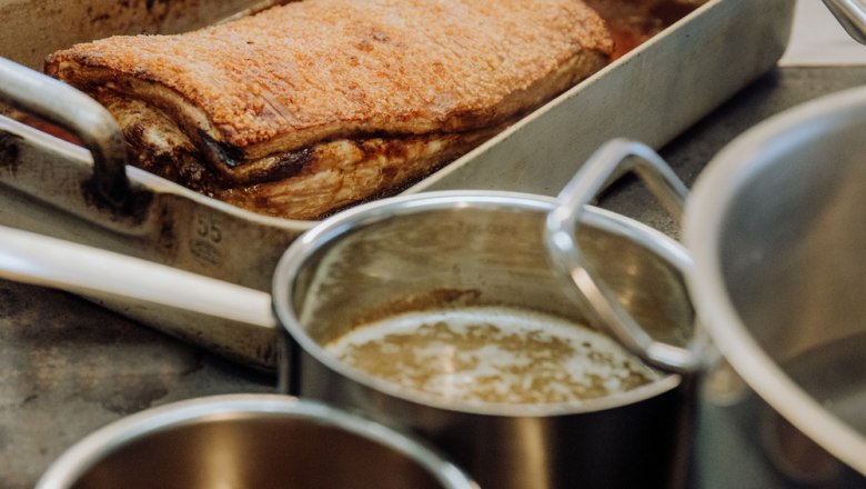 Knuspriger Schweinsbraten in einer Metallpfanne, daneben Töpfe mit Soße.
