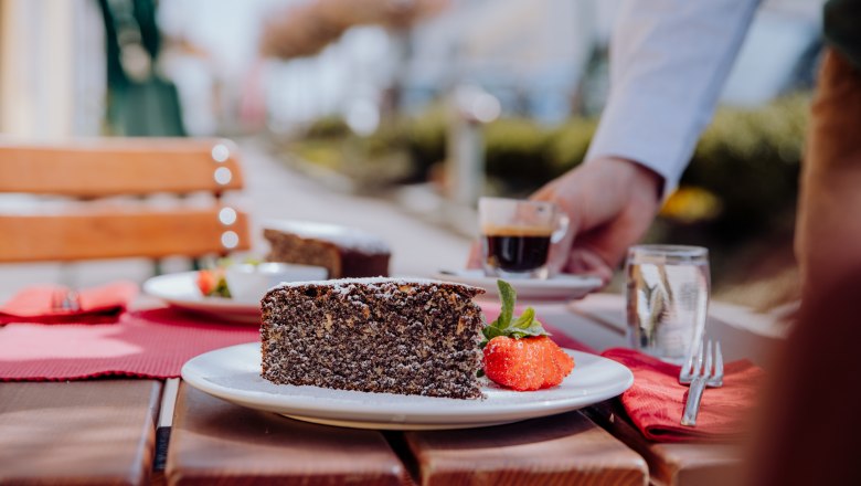 Mohnkuchen mit Erdbeere und Espresso auf einem Holztisch im Freien serviert.