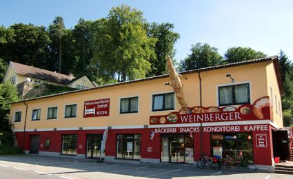 Außenansicht einer Bäckerei mit gelber Fassade und rotem Schild.
