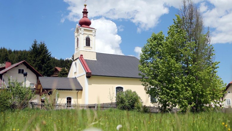Kirche in Mitterbach mit rotem Turm und gr&uuml;nem Baum im Vordergrund.