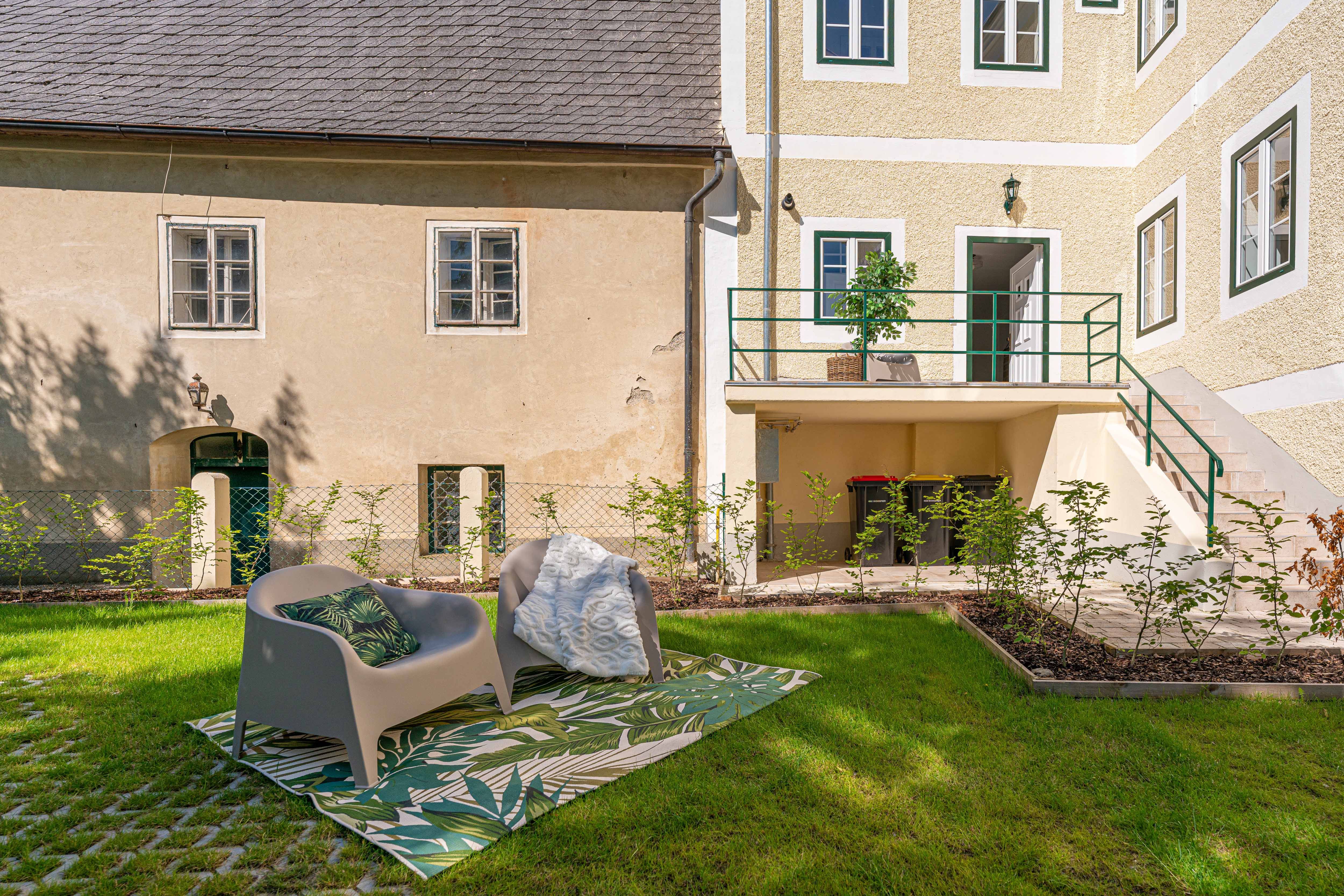 Garten mit Sitzgelegenheit vor einem alten Gebäude mit gelber Fassade und grünen Fensterrahmen.