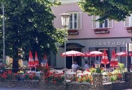 Außenansicht eines Gasthofs mit Terrasse, roten Sonnenschirmen und Blumendekoration.