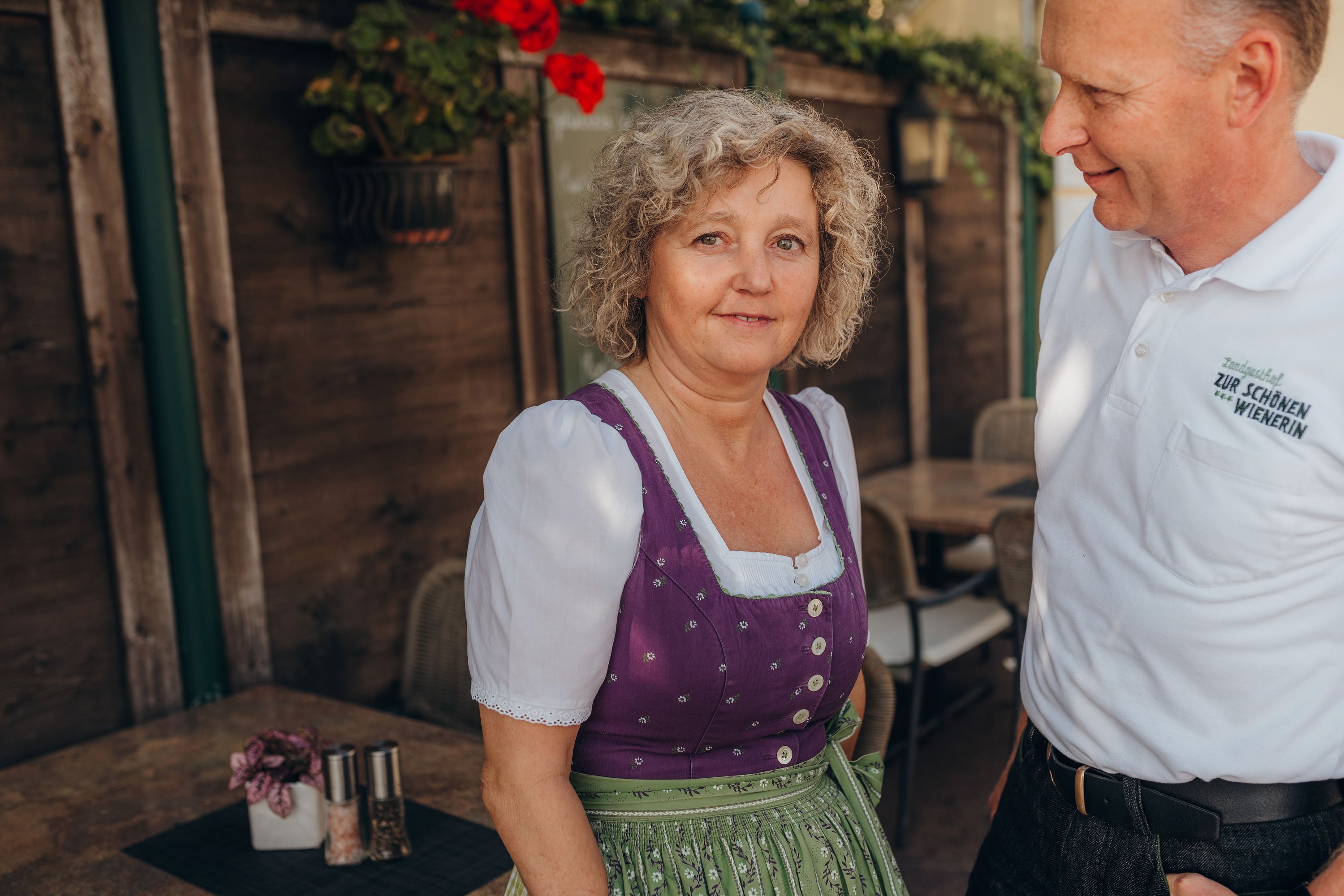 Eine Frau in traditioneller Kleidung steht neben einem Mann in einem weißen Hemd mit Aufschrift.