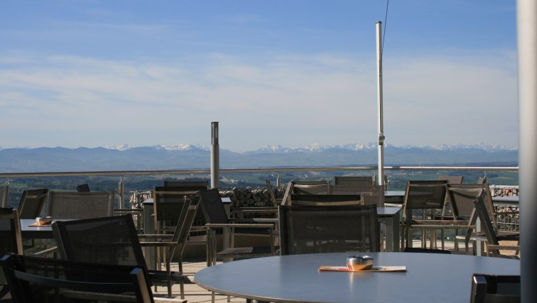 Terrasse mit Tischen und Stühlen, im Hintergrund Alpenpanorama.
