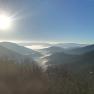 Blick von einem Berg auf nebelverhangene T&auml;ler und H&uuml;gel unter strahlend blauem Himmel mit Sonnenschein.