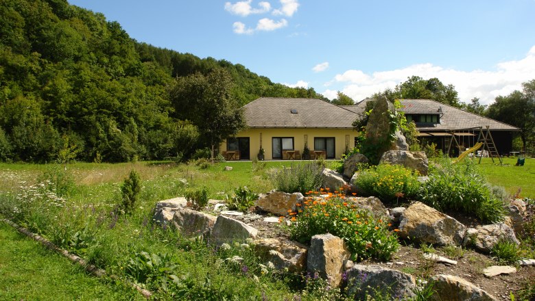 Ein gelbes Haus mit Garten und Felsen im Vordergrund, umgeben von Bäumen.