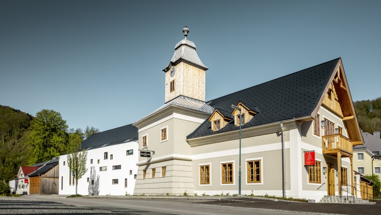 Ein modernes Gebäude mit Glockenturm und Holzverkleidung, umgeben von Bäumen und klarem Himmel.