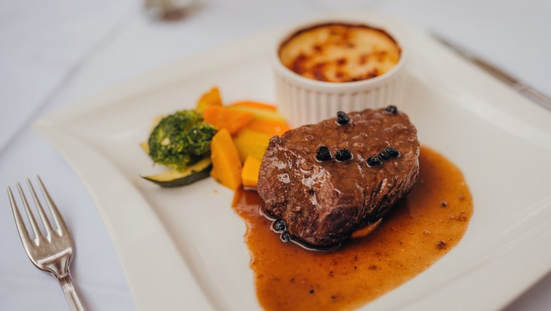 Ein Pfeffersteak mit Sauce, Gemüse und Kartoffelgratin auf einem weißen Teller.