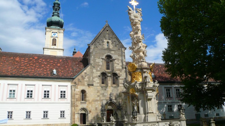 Innenhof des Stifts Heiligenkreuz mit barocker S&auml;ule und Kirchturm.