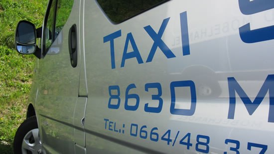 Nahaufnahme eines silbernen Taxis mit blauer Aufschrift und Telefonnummer.