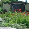 Bl&uuml;hender Garten mit roten Mohnblumen vor einem Geb&auml;ude mit Holztor.