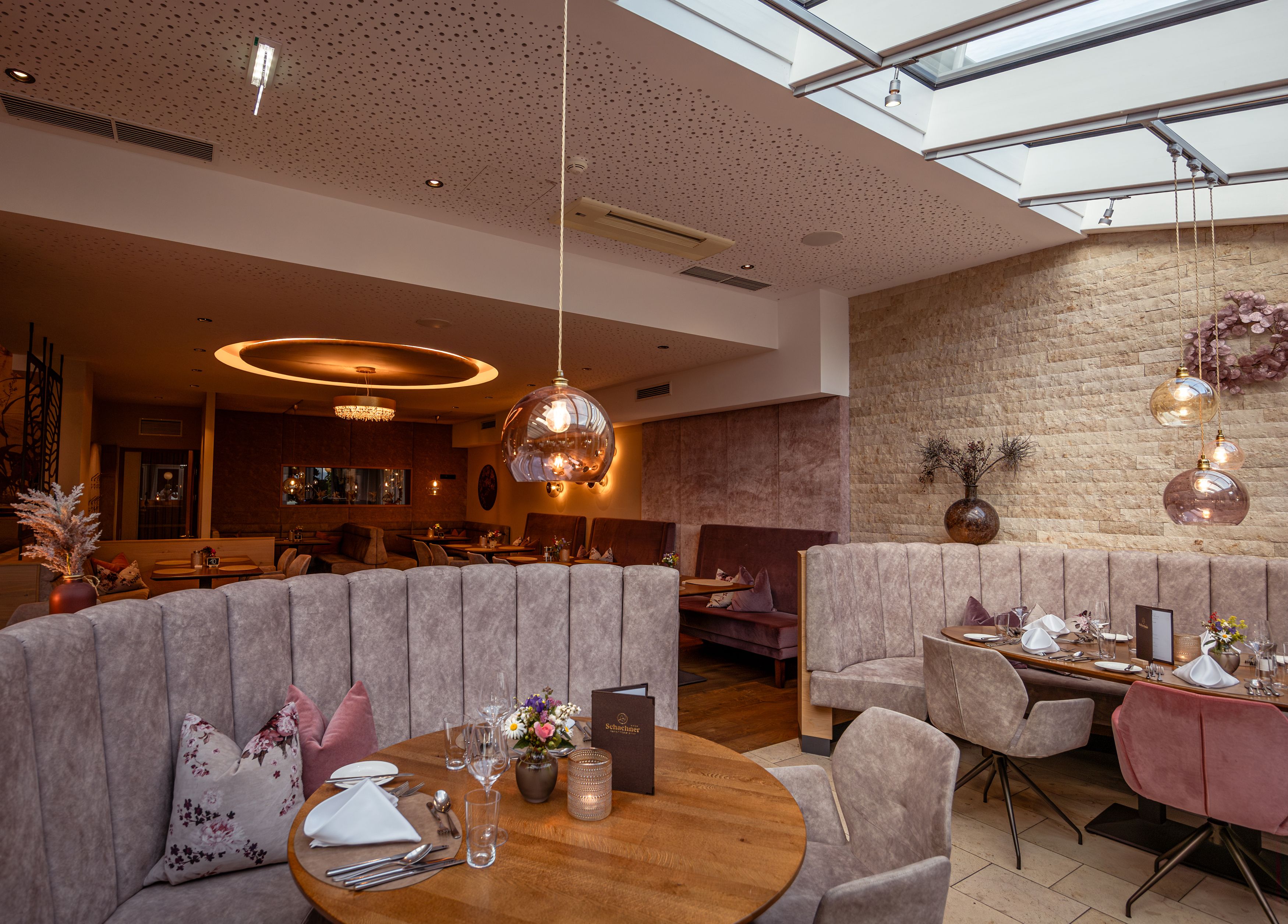 Elegantes Restaurant mit moderner Einrichtung, runden Tischen und gepolsterten Sitzbänken unter einem Glasdach.