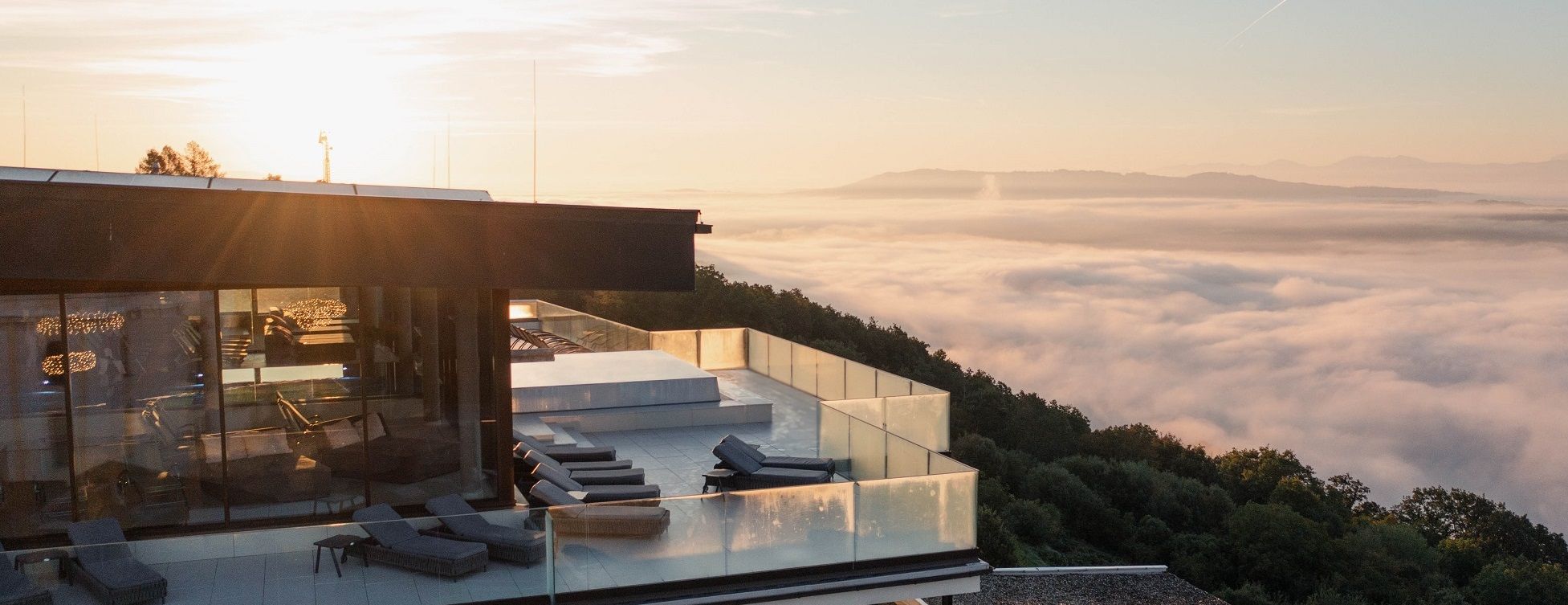 Modernes Gebäude mit Terrasse über einem Nebelmeer bei Sonnenaufgang.
