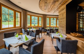 Elegantes Restaurant mit Holzelementen, gedeckten Tischen und gro&szlig;en Fenstern mit Blick ins Gr&uuml;ne.