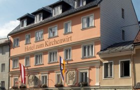 Fassade des Hotels zum Kirchenwirt mit Fahnen und blauer Himmel.