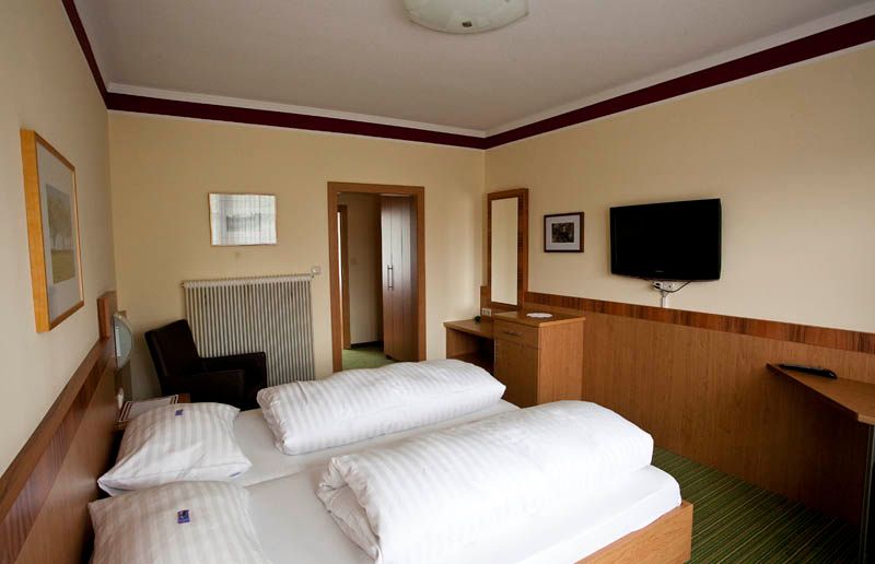 Hotelzimmer mit Doppelbett, TV, Schreibtisch und Spiegel.