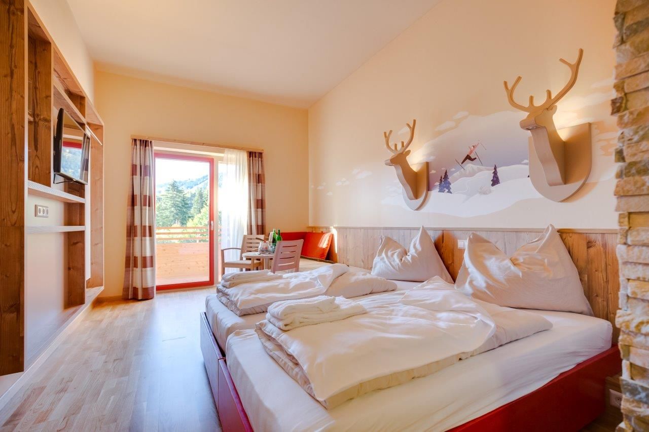 Hotelzimmer mit Doppelbett, Holzmöbeln und Balkon mit Bergblick.