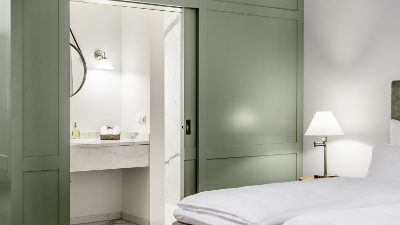 Hotelzimmer mit grünem Schiebetürenschrank, Bett und Blick ins Badezimmer.