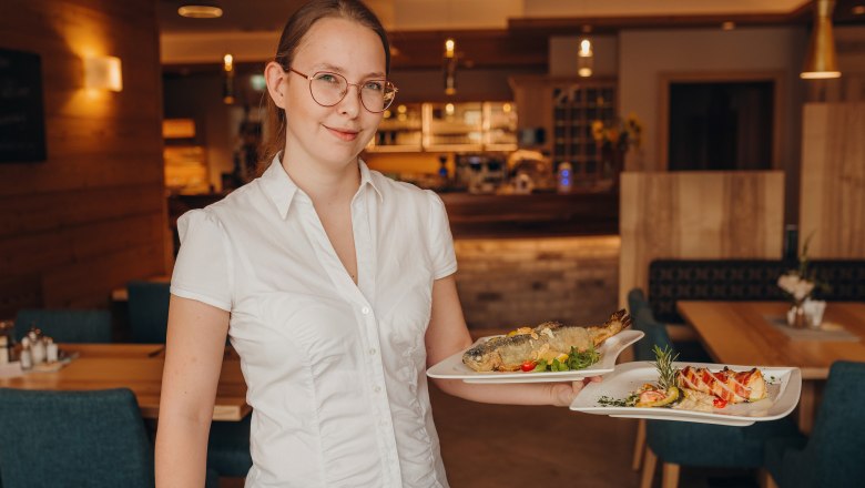 Eine Frau in einem Restaurant trägt zwei Teller mit Speisen.