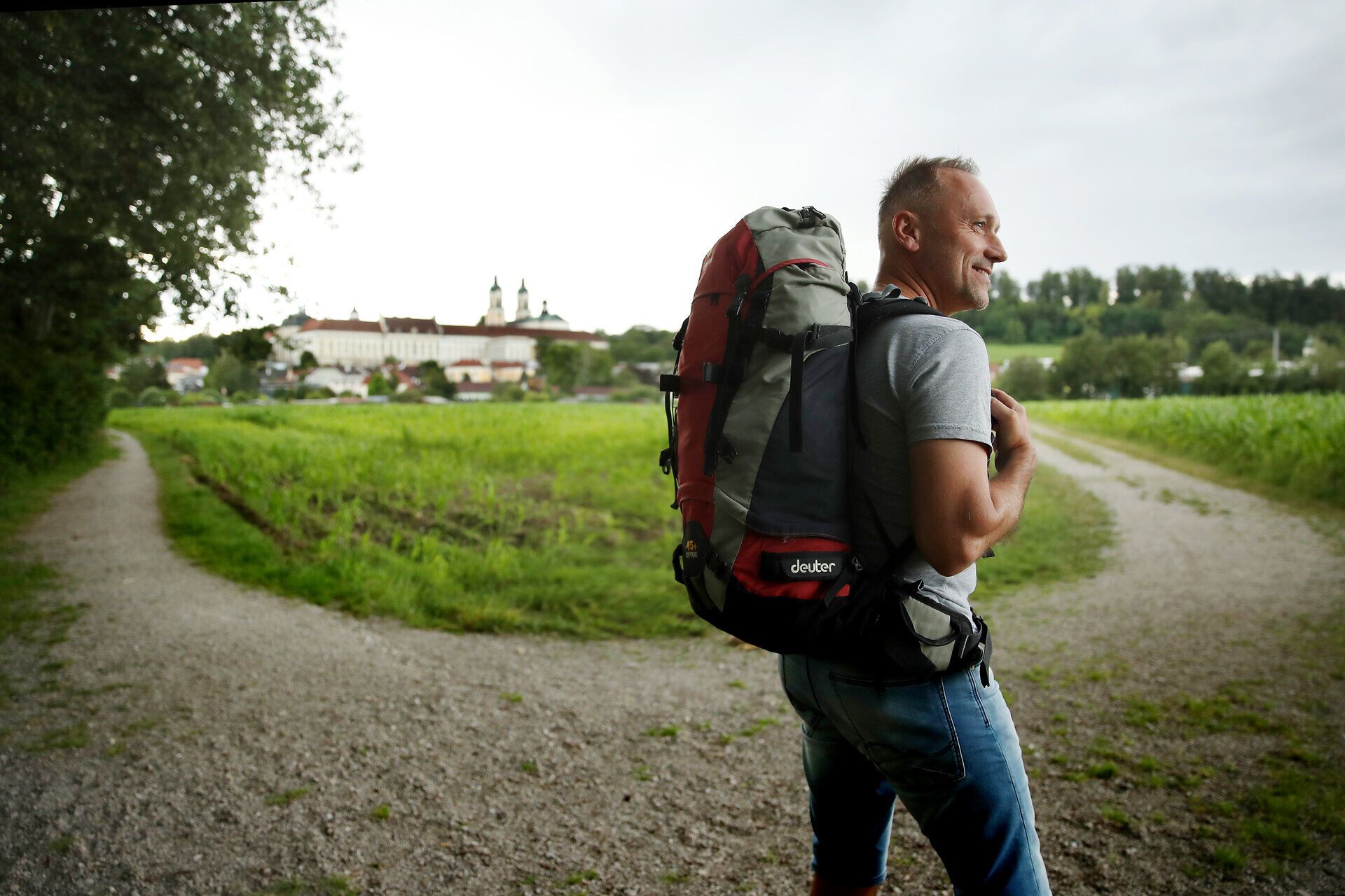 Pilger mit Rucksack auf Feldweg vor Stift St. Florian.