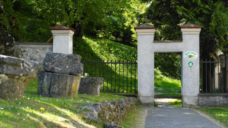 Steintor mit Garten im Hintergrund, umgeben von Bäumen.