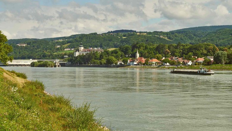 Flusslandschaft mit Dorf und Hügeln im Hintergrund.