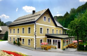 Ein gelbes Gasthaus mit Terrasse und Sonnenschirmen, umgeben von B&auml;umen.