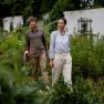 Ein Mann und eine Frau spazieren durch einen grünen Garten, umgeben von Pflanzen.