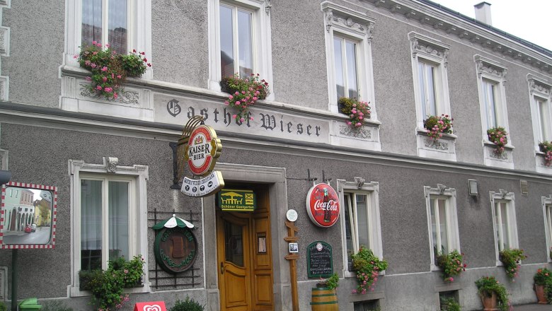 Fassade des Gasthofs Wieser mit Blumenk&auml;sten und Werbeschildern.