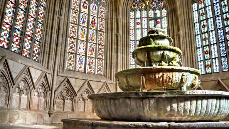 Ein alter Brunnen in einem gotischen Geb&auml;ude mit bunten Glasfenstern.